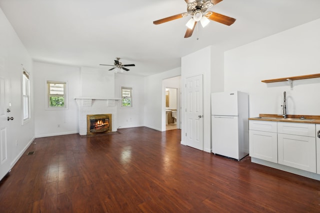 unfurnished living room with sink, dark hardwood / wood-style floors, ceiling fan, and a fireplace