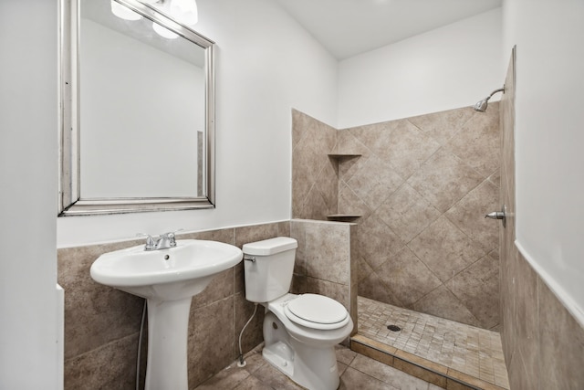 bathroom featuring a tile shower, tile walls, toilet, and tile floors