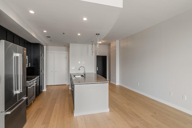 kitchen featuring sink, light stone counters, light hardwood / wood-style floors, a center island with sink, and high end appliances