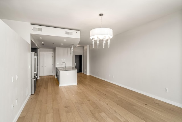 interior space featuring light hardwood / wood-style flooring, stainless steel fridge, decorative light fixtures, a kitchen island with sink, and white cabinets