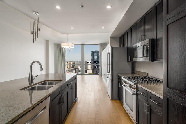 kitchen featuring appliances with stainless steel finishes, light stone counters, sink, pendant lighting, and light hardwood / wood-style floors