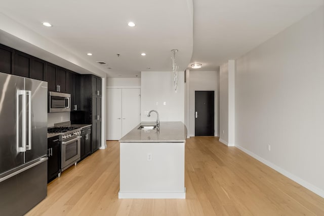 kitchen with light stone countertops, sink, light hardwood / wood-style flooring, a center island with sink, and high end appliances