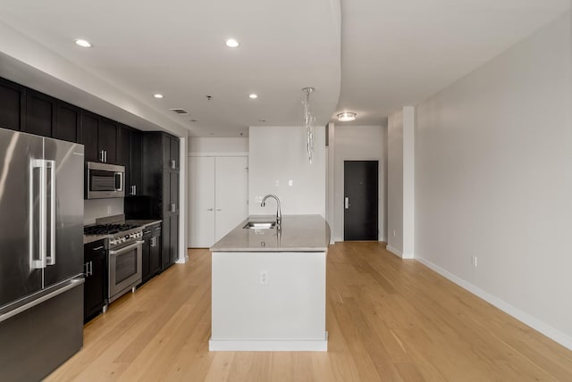 kitchen featuring light stone countertops, a kitchen island with sink, sink, light hardwood / wood-style flooring, and high quality appliances