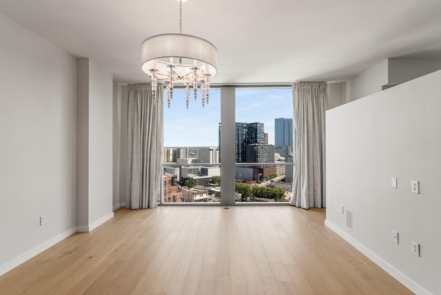 spare room with expansive windows, light wood-type flooring, and a notable chandelier