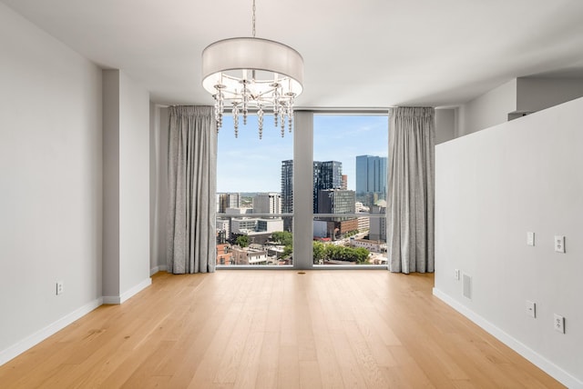 spare room featuring wood-type flooring, expansive windows, and a notable chandelier