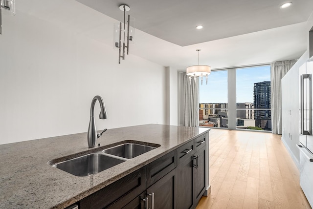 kitchen with light stone countertops, sink, decorative light fixtures, a wall of windows, and a notable chandelier