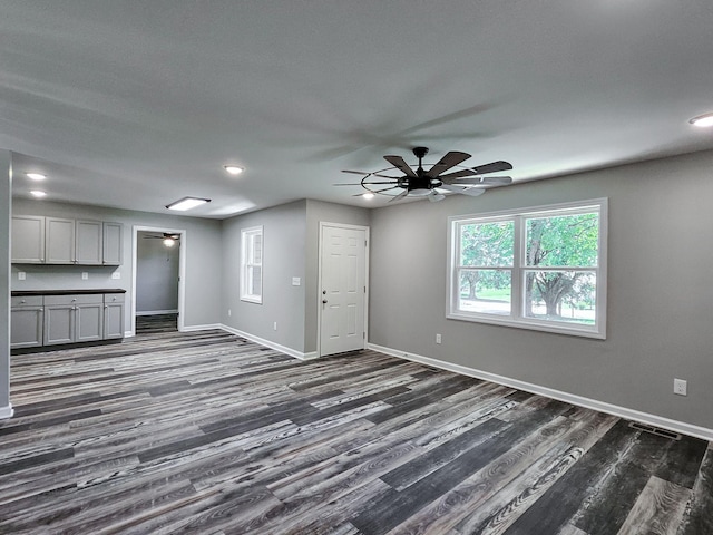 unfurnished living room featuring dark wood-type flooring and ceiling fan