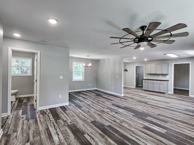 unfurnished living room featuring dark wood-type flooring and ceiling fan with notable chandelier