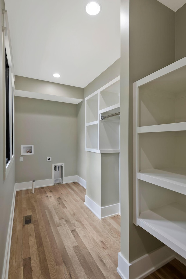 clothes washing area featuring hookup for an electric dryer, hookup for a washing machine, light hardwood / wood-style flooring, and built in shelves