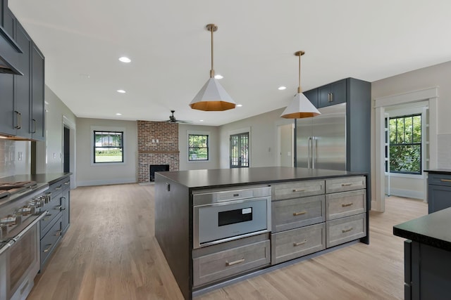 kitchen featuring decorative light fixtures, a brick fireplace, ceiling fan, premium appliances, and light hardwood / wood-style floors