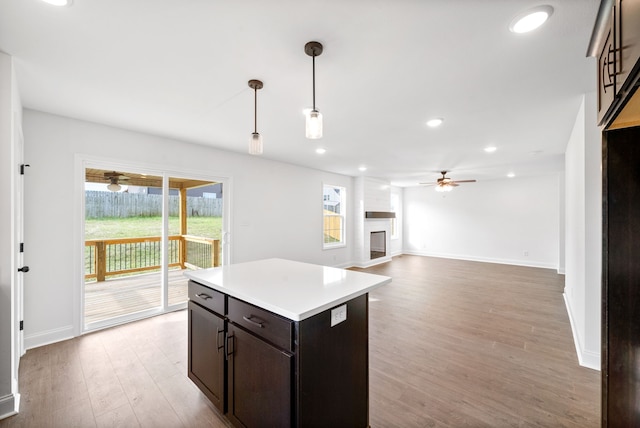 kitchen featuring ceiling fan, a large fireplace, light hardwood / wood-style flooring, decorative light fixtures, and dark brown cabinets