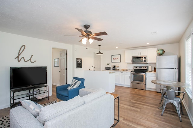 living room featuring ceiling fan, light wood-type flooring, and sink