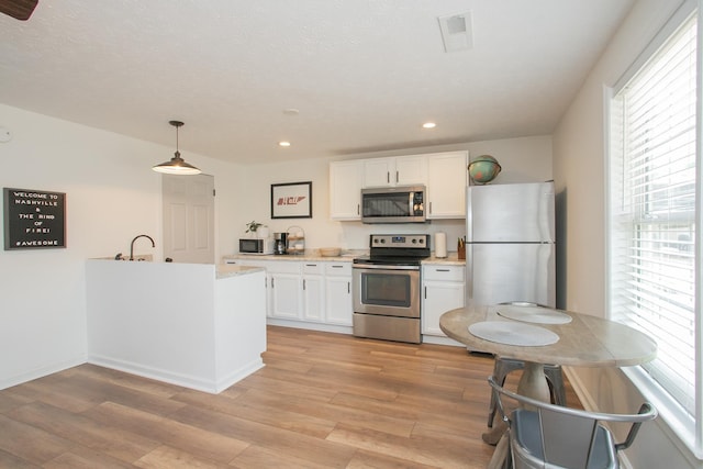 kitchen featuring appliances with stainless steel finishes, light hardwood / wood-style flooring, white cabinets, and hanging light fixtures