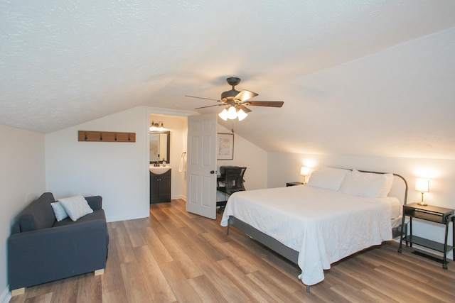 bedroom with ceiling fan, ensuite bathroom, vaulted ceiling, wood-type flooring, and a textured ceiling