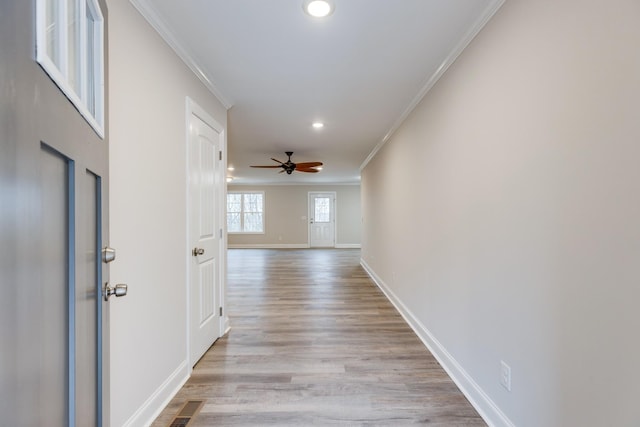 hallway featuring baseboards, light wood-type flooring, visible vents, and crown molding