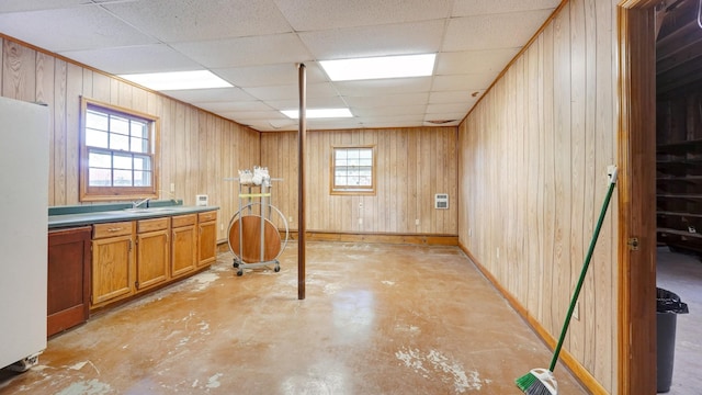 basement featuring a paneled ceiling, white refrigerator, sink, and wooden walls