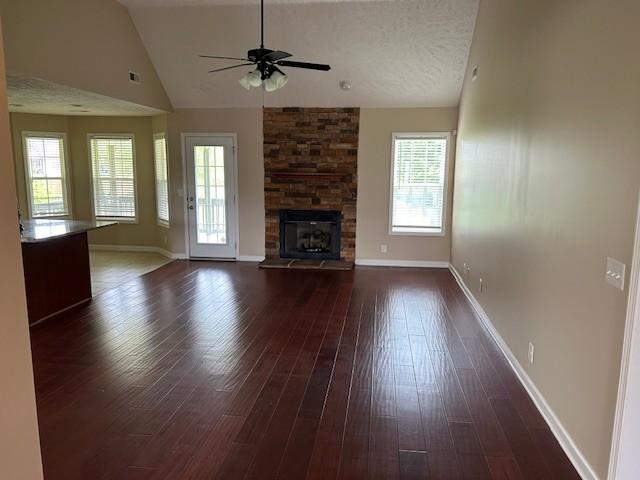 unfurnished living room featuring ceiling fan, dark hardwood / wood-style flooring, a stone fireplace, and vaulted ceiling