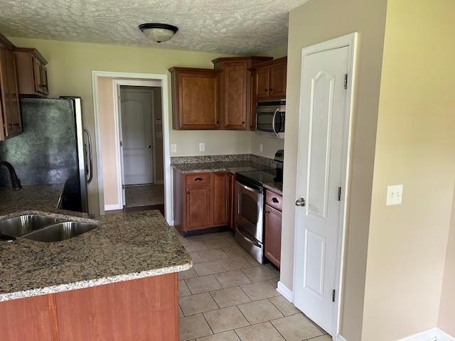 kitchen with sink, dark stone countertops, light tile patterned floors, a textured ceiling, and appliances with stainless steel finishes