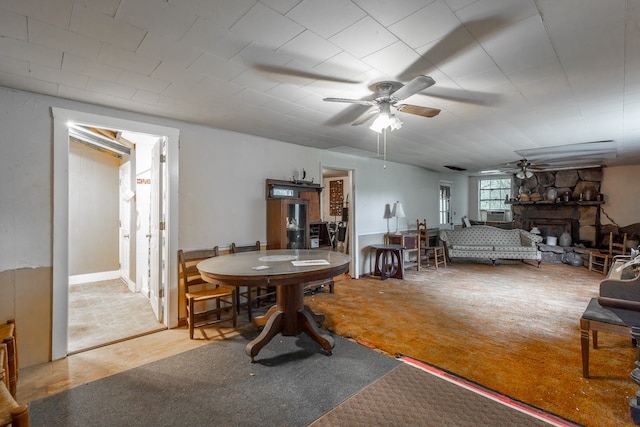 carpeted dining room with a stone fireplace and ceiling fan