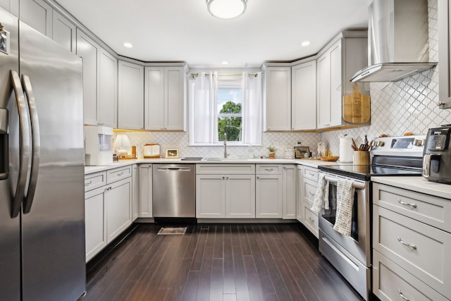 kitchen featuring stainless steel appliances, wall chimney exhaust hood, dark hardwood / wood-style floors, and tasteful backsplash