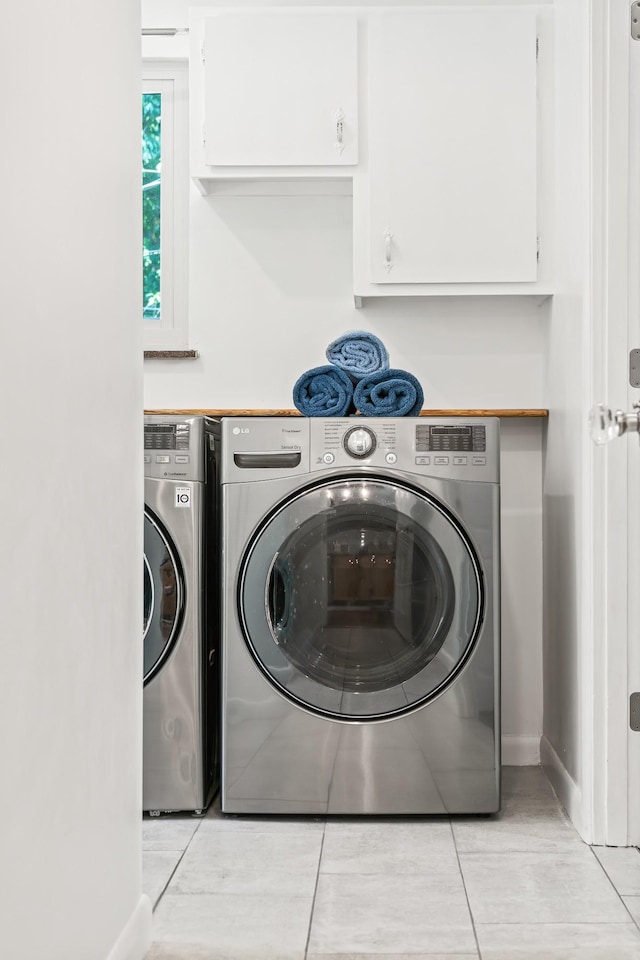 clothes washing area featuring separate washer and dryer, light tile patterned floors, and cabinets