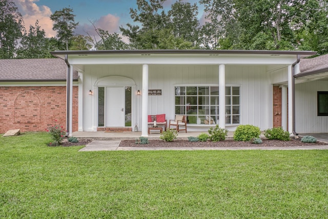 back house at dusk with covered porch and a lawn