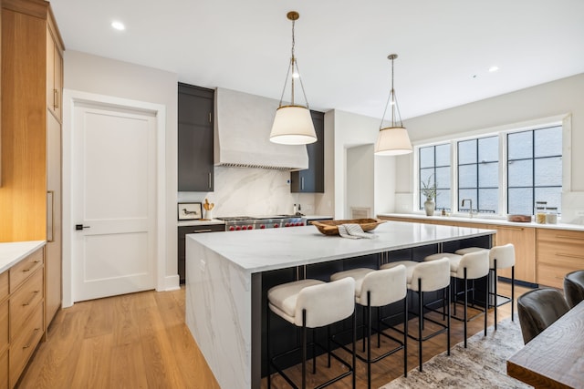 kitchen featuring light hardwood / wood-style flooring, premium range hood, light brown cabinetry, light stone countertops, and a center island