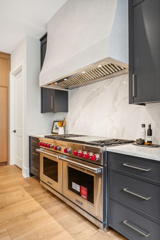 kitchen with decorative backsplash, double oven range, premium range hood, and light hardwood / wood-style flooring