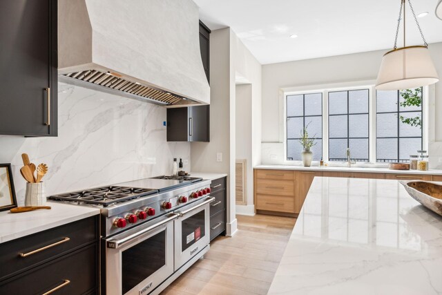 kitchen featuring double oven range, premium range hood, tasteful backsplash, light stone counters, and pendant lighting