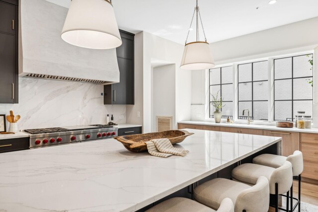 kitchen with backsplash, custom range hood, hanging light fixtures, light stone countertops, and hardwood / wood-style flooring