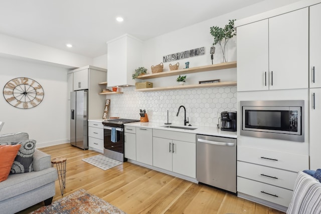 kitchen with tasteful backsplash, white cabinetry, sink, stainless steel appliances, and light hardwood / wood-style flooring