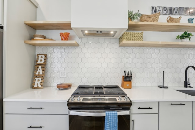 kitchen featuring stainless steel range with gas cooktop, range hood, white cabinetry, sink, and backsplash