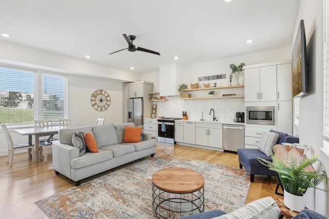 living room featuring ceiling fan, sink, and light wood-type flooring