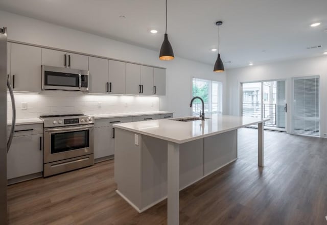 kitchen featuring a kitchen island with sink, hanging light fixtures, stainless steel appliances, and sink