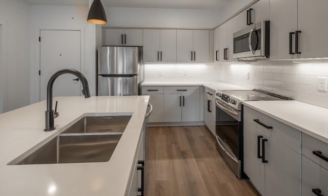 kitchen with sink, dark wood-type flooring, tasteful backsplash, pendant lighting, and appliances with stainless steel finishes