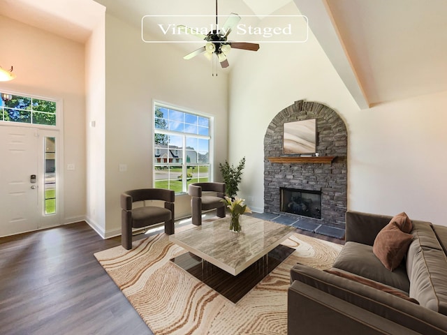 living room featuring ceiling fan, a stone fireplace, dark wood-type flooring, and a wealth of natural light