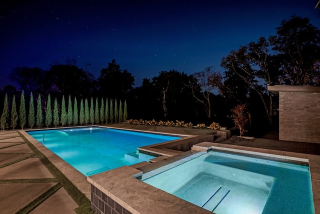 pool at night featuring an in ground hot tub