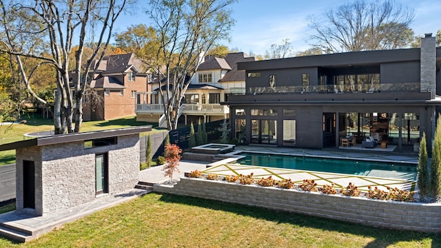 rear view of property with a balcony, a lawn, a swimming pool with hot tub, and a patio area