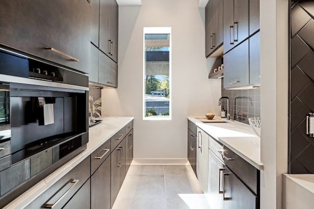 kitchen featuring light stone counters, sink, oven, light tile patterned flooring, and tasteful backsplash