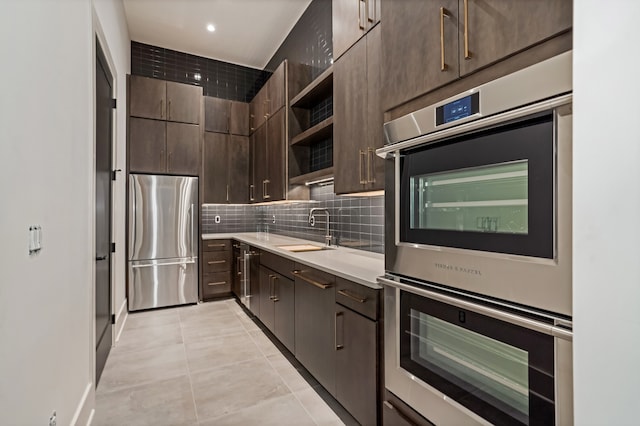 kitchen featuring sink, light tile patterned floors, backsplash, dark brown cabinetry, and appliances with stainless steel finishes