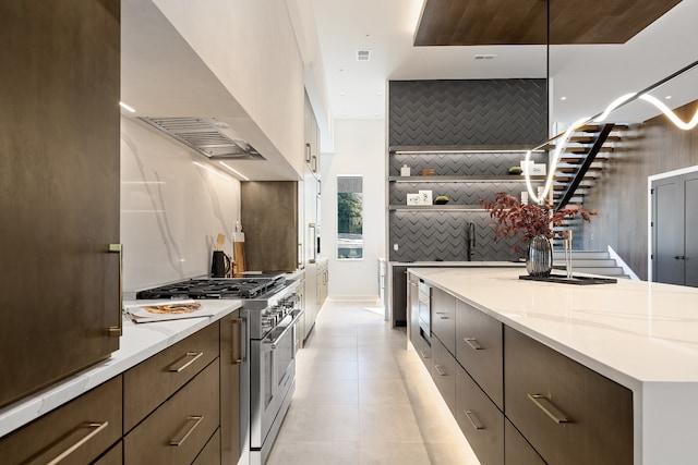 kitchen with light stone counters, decorative backsplash, stainless steel stove, and wall chimney exhaust hood