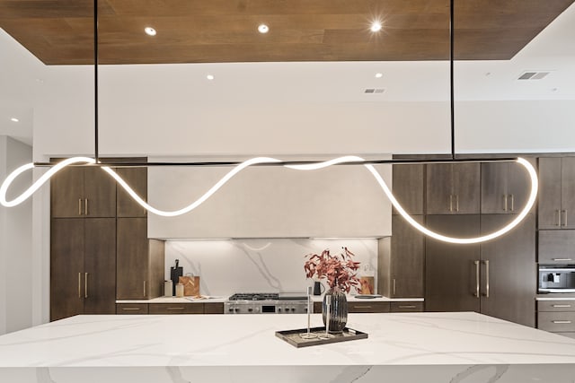 kitchen with wood ceiling, a center island, stainless steel gas cooktop, light stone countertops, and dark brown cabinets