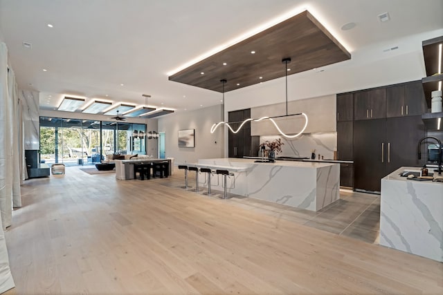 kitchen with decorative light fixtures, a large island, ceiling fan, light wood-type flooring, and light stone countertops