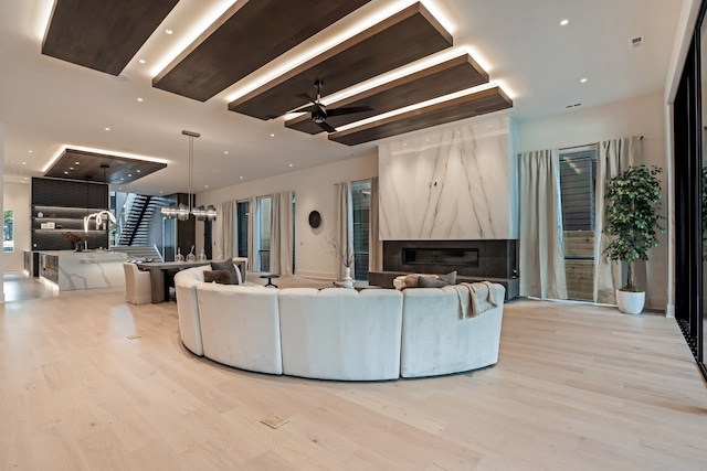 living room with a high end fireplace, ceiling fan, and light hardwood / wood-style floors