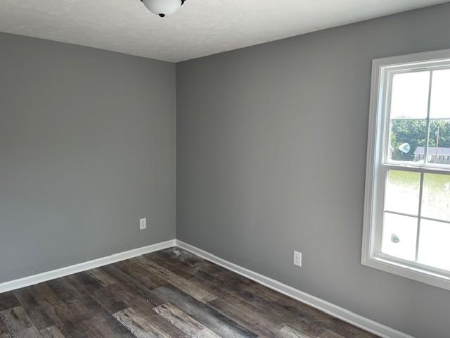 empty room with dark wood-type flooring and baseboards