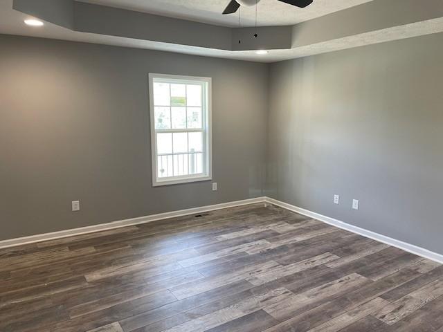 empty room featuring a raised ceiling, ceiling fan, and dark wood-style flooring