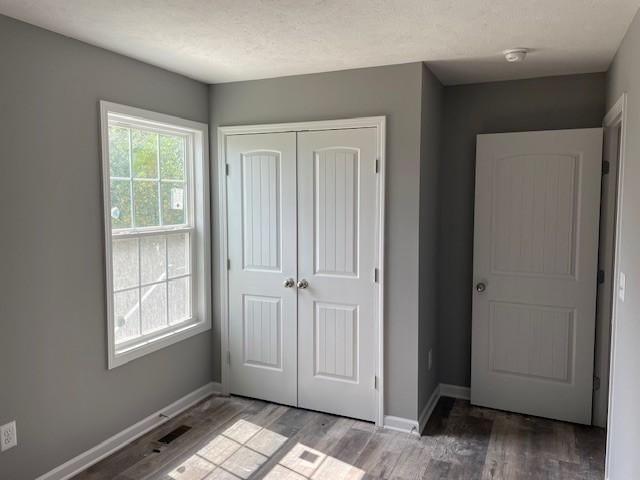 unfurnished bedroom with a closet, visible vents, wood finished floors, and baseboards