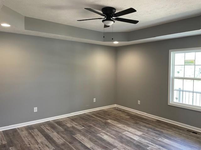 empty room with dark wood finished floors, visible vents, ceiling fan, and baseboards
