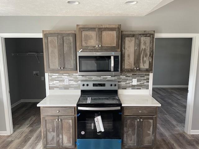 kitchen with appliances with stainless steel finishes, tasteful backsplash, dark wood-style floors, and baseboards