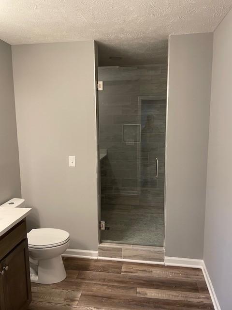full bath with wood finished floors, a shower stall, toilet, vanity, and a textured ceiling